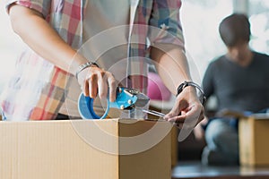 Concept young couple moving house. Close-up hand of woman use tape sealing cardboard box