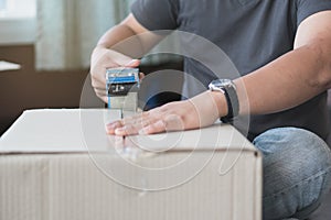 Concept young couple moving house. Close-up hand of woman use tape sealing cardboard box