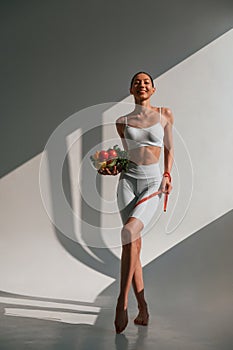 Conception of diet. With vegetalbes and fruits. Young caucasian woman with slim body shape is indoors in the studio photo