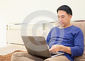 Concepts technology with People lifestyle. Asian man working on laptop computer and talking mobile phone on the bed