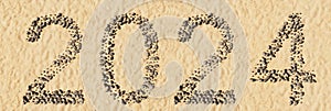 Conceptual 2024 year made of stones on beach sand handmade symbol shape, golden sandy background.