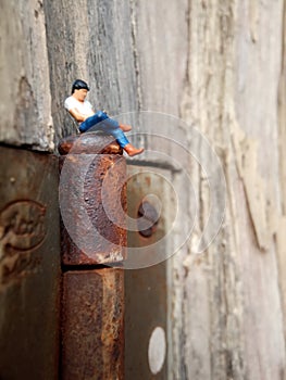 Conceptual Close Up Photo, Gadget Addicted young Man, Holding Smartphone, sitting at corrosive door hinge, under barbed wire