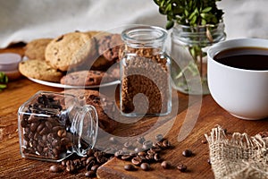 Conceptual composition with two jars of coffee beans, instant coffee and tasty cookies on wooden table, selective focus