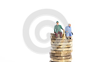 Miniture figure retired couple sat on a stack of pound coins photo
