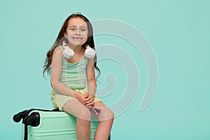 Conceptual emotional portrait of a lovely little child girl making faces, smiling looking at camera, sitting on suitcase