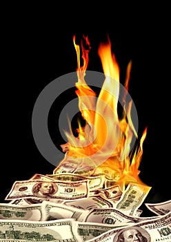 Conceptual finance image of burning pile of money, dollar bills, and fire flames in black background