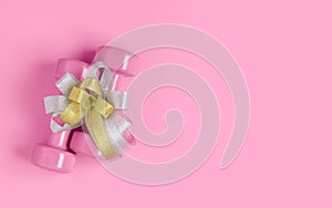 Conceptual fitness and healthy sport background with two pink dumbbell with gift bow on pink background. Flat lay top view with