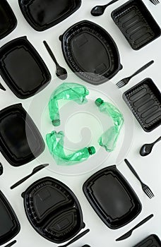 Conceptual flatlay with new empty black containers, forks, spoons and recycle symbol made of used green plastic bottles