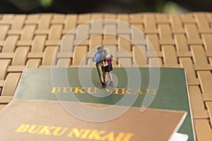 Conceptual illustration photo for Lovely moment, Young Couple Mini figure Toy kissing beyond Buku Nikah, or Indonesia Wedding