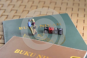 Conceptual illustration photo for Lovely moment, Young Couple Mini figure Toy kissing beyond Buku Nikah, or Indonesia Wedding