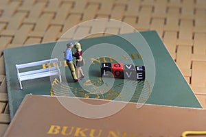 Conceptual illustration photo for Lovely moment, Young Couple Mini figure Toy kissing beyond Buku Nikah, or Indonesia Wedding