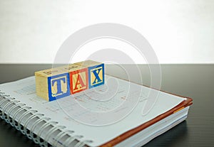 Conceptual image of annual tax return. Stacked wooden block letter forming TAX on dark reflective surface. Focus at block letter A