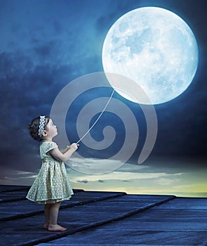 Conceptual image of a baby holding a moon-balloon