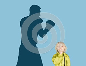 Conceptual image with boy and shadow of sportive male boxer, champion on blue background. Childhood, dreams, imagination