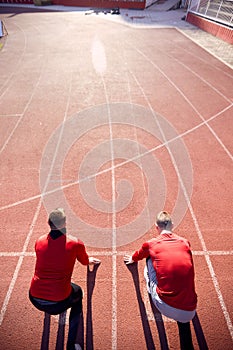 Conceptual image of competition. Two caucasian men at starting line of athletic track ready to start the race