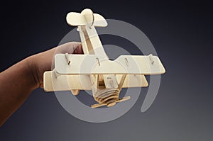 Conceptual image of cropped hand holding toy wooden retro airplane on dark background
