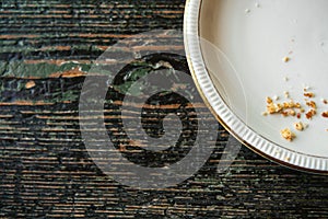 Conceptual image of the end of the holiday is an empty plate with crumbs on a wooden surface.