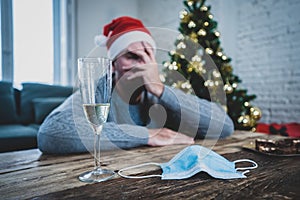 Conceptual image of Face mask and champagne glass in blur background of depressed man at christmas