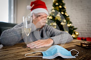 Conceptual image of Face mask and champagne glass in blur background of depressed man at christmas