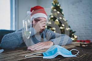 Conceptual image of Face mask and champagne glass in blur background of depressed man at christmas