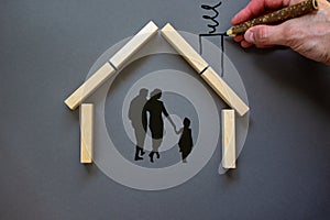 Conceptual image of family values and adoption. House from wooden blocks on beautiful grey background. Male hand draws with black