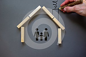 Conceptual image of family values and adoption. House from wooden blocks on beautiful grey background. Male hand draws with black