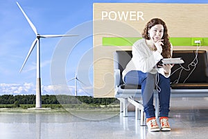 Conceptual image of green energy, charging station in airport lounge with windmill generator, woman recharging devices