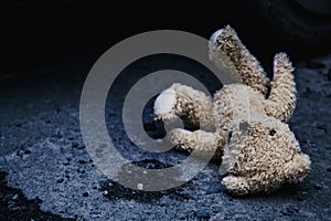Conceptual image: lost childhood, loneliness, pain and depression. Dirty toy Teddy bear lying down outdoors. Copy space for text
