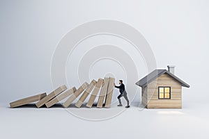 A conceptual image of a man preventing a falling row of dominoes from crashing into a small house, symbolizing protection and