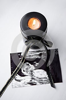 Conceptual image of mourning, miscarriage, pregnancy loss or grief counseling. Ultrasound picture of baby next to candle.