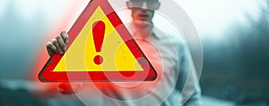 Conceptual image of a person holding a floating exclamation mark in a warning triangle, symbolizing caution, alertness, and