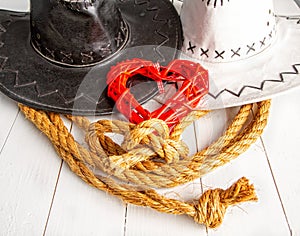 Conceptual image of rural wedding of cowboys. White bride hat and dark groom hat and red heart symbol of love