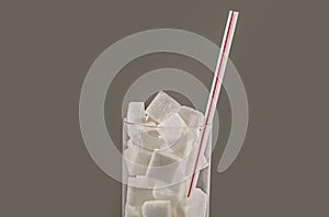 Conceptual macro still life image of refreshment glass full of sugar cubes and straw isolated on white background in glucose addic