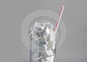 Conceptual macro still life image of refreshment glass full of sugar cubes and straw on white background in glucose addic