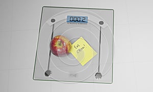 Conceptual and modern still life delicious apple and yellow posit note text saying eat clean stuck on bathroom scale in weight