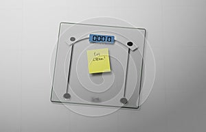 Conceptual and modern still of yellow handwritten posit note saying eat clean stuck on bathroom scale in weight loss dieting and photo