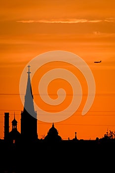 Conceptual photo of city downtown at sunset with skyline silhouette against a beautiful orange sky a airplane. Defocused