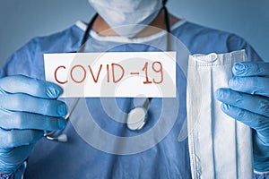 Conceptual photo for COVID-19 epidemic.Doctor holding medical mask and a white papaer with Covid-19 written