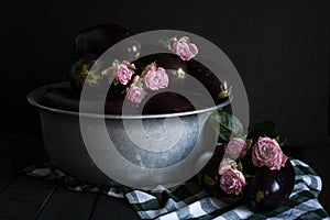 Conceptual photo: dark eggplants lie in aluminum bowl decorated with flowers. Dark key