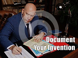 Conceptual photo about Document Your Invention Male office workers with yellow shirt holding and writing documents on office desk