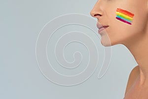 Conceptual photo of female face with colorful painted rainbow on cheek. LGBT flag. Equality and support of diversities to people