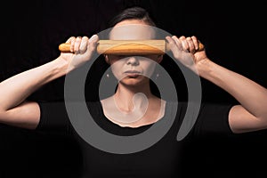 Conceptual photo with a girl and a rolling pin. Girl closes her mouth with a rolling pin. A woman in an everyday household routine