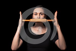 Conceptual photo with a girl and a rolling pin. Girl closes her mouth with a rolling pin. A woman in an everyday household routine