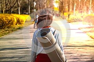 Conceptual photo about a healthy lifestyle and sports. Girl with a Mat for fitness in the Park at sunset.