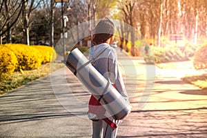 Conceptual photo about a healthy lifestyle and sports. Girl with a Mat for fitness in the Park at sunset.