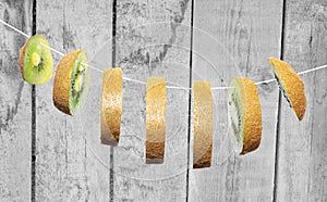 Conceptual photo of a kiwi. Cut into slices kiwi hanging on a white rope