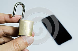 Conceptual photo of security on mobile phones. Hand holding a open padlock and a cell phone in the background