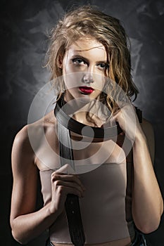 Conceptual photo of a young girl with disheveled wet hair, naked shoulders, aggressive make-up, and a men`s leather belt around