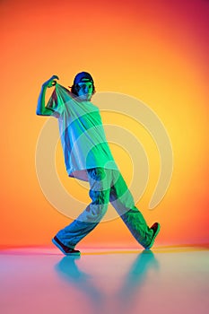 Conceptual portrait of young man, hip-hop dancer in stylish clothes in action isolated on colorful background at dance