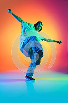 Conceptual portrait of young man, hip-hop dancer in stylish clothes in action isolated on colorful background at dance